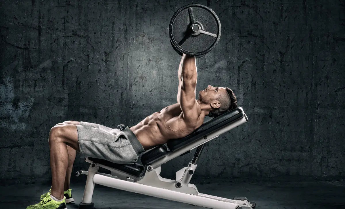 Homme musclé effectuant un développé incliné avec un haltère sur un banc de musculation, sur fond de mur en béton.