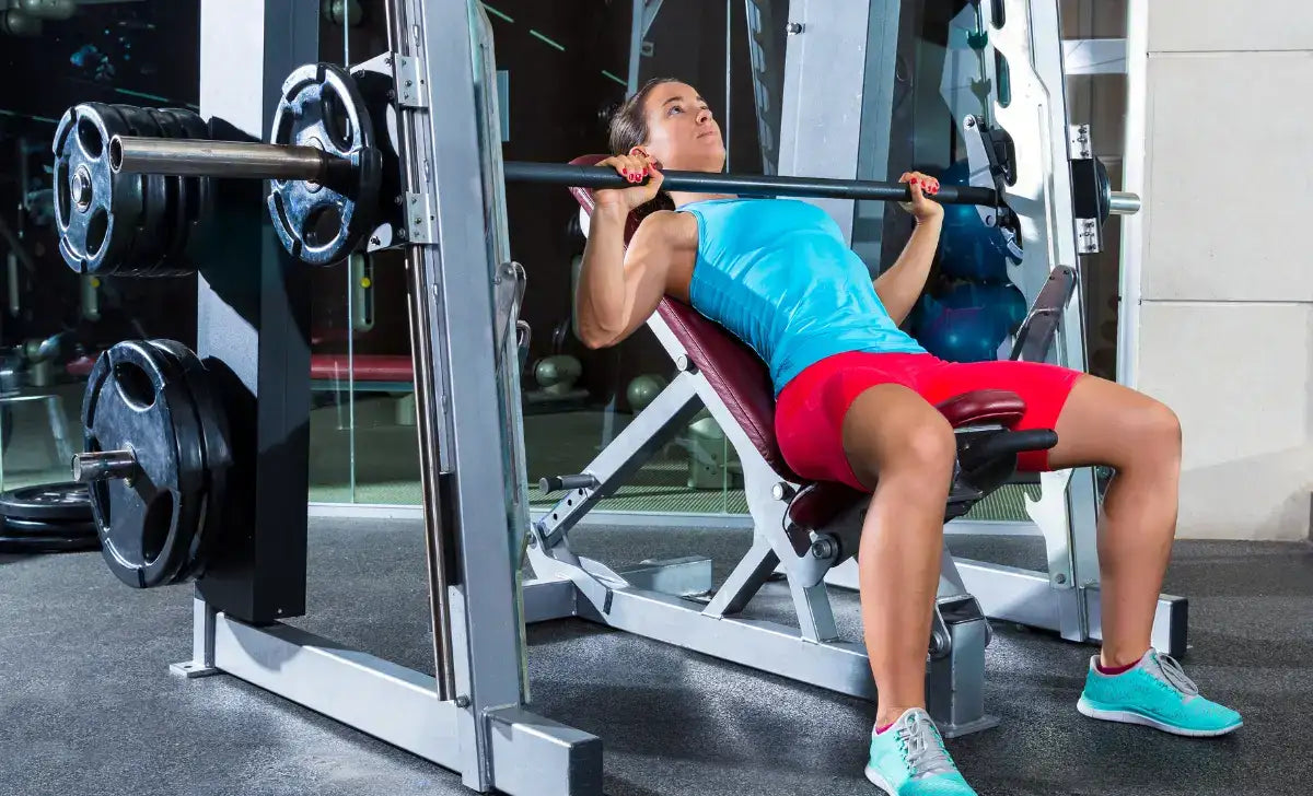 Femme effectuant un développé couché incliné à la Smith machine pour cibler les pectoraux supérieurs